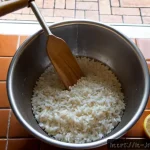 스시용 밥 짓는 법 - Photorealistic overhead view of an Italian home kitchen, hands rinsing glossy short-grain rice in a ...